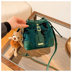 Détail du sac seau en velours vert foncé avec motif matelassé et pendentif ours en peluche