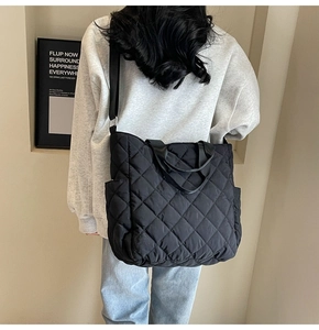 Detail of black quilted tote bag with diamond pattern and adjustable shoulder strap