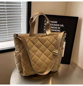 Detail of khaki quilted tote bag with adjustable strap on a modern metallic surface