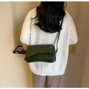 Detail of dark green underarm bag with gold buckle on a model in minimalist studio