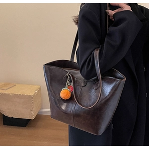 Close-up of vintage brown leather tote bag with orange persimmon charm on shoulder