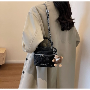 Detail of black quilted chain bag with plush monster charm on khaki trench coat