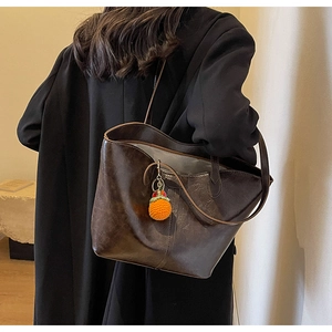 Close-up of dark brown leather tote bag with orange knitted charm on female model