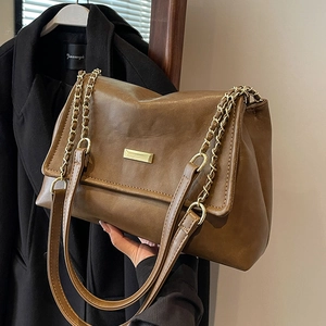 Brown leather tote bag with gold chain strap shown in a stylish lifestyle setting