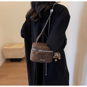 Detail of coffee quilted crossbody bucket bag with chain strap and plush monster charm