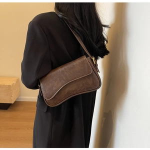 Detail of vintage brown leather shoulder bag with textured finish on a black wool coat