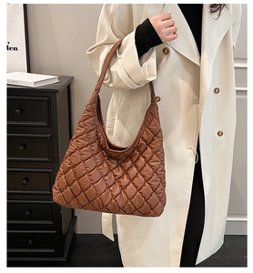 Detail of a brown quilted tote bag showing plush puffy texture and long shoulder strap
