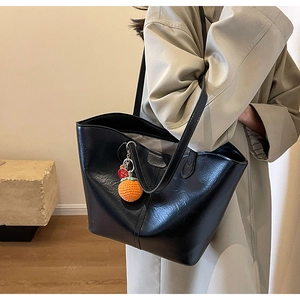 Detail of black faux leather tote bag with a unique crochet orange charm on the strap