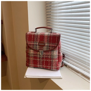 Detail of red and white plaid tweed backpack featuring brown leather handle and metal buckle