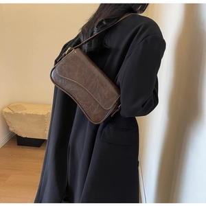 Close-up of retro dark brown leather underarm bag with wavy flap on model's shoulder