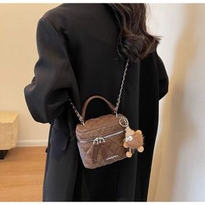 Detail of a brown quilted mini box bag featuring a plush charm and sleek metal chain strap