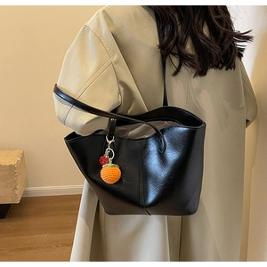 Close-up of black glossy tote bag with leather texture and handmade orange pendant