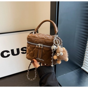 Detailed close-up of brown quilted velvet mini bucket bag with chain and bear charm