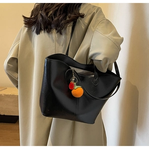 Detail of black matte tote bag with orange knit charm on model in beige trench coat