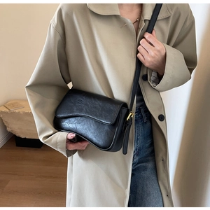 Detail of vintage black leather crossbody bag with asymmetric flap and gold hardware