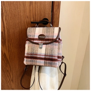 Close-up of pink plaid mini backpack with brown leather trim hanging on a wooden handle