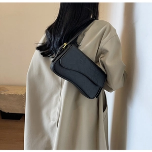 Close-up of black pleated underarm bag with smooth curved silhouette and gold buckle detail