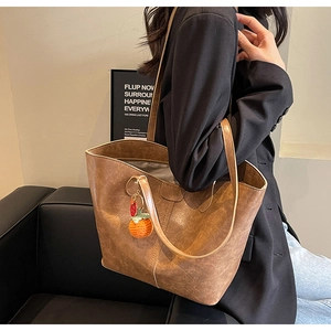 Detail view of the retro brown leather tote bag with a small orange knitted pendant charm