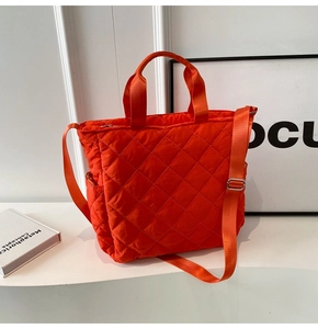 Detailed close-up of bright orange quilted nylon tote bag with adjustable shoulder strap