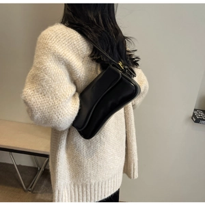 Detail of a black leather underarm bag with adjustable strap on a knit sweater