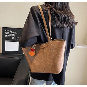 Rear view of model wearing a vintage brown faux leather tote bag with orange pompom detail