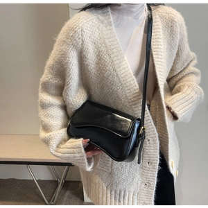 Detail of a large black leather shoulder bag with gold buckles on a beige knit sweater