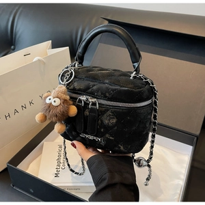 Close-up of black quilted bucket bag with chain strap and cute plush monster charm