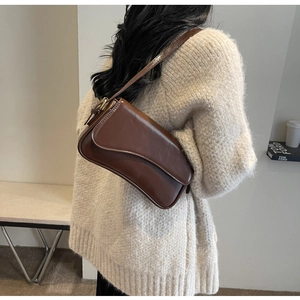 Detail of a brown leather saddle bag styled with a beige sweater for a trendy autumn look
