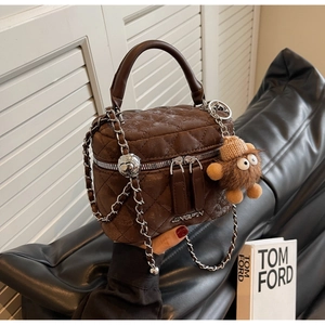 Detail of dark brown quilted vanity bag with chain strap and teddy bear charm