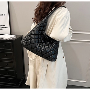 Close-up of black quilted puffer tote bag worn by a model in a minimalist stylish setting