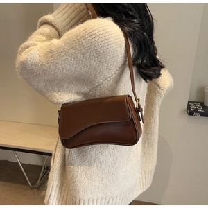 Detail of vintage dark brown shoulder bag with a unique wavy edge flap on knit sweater