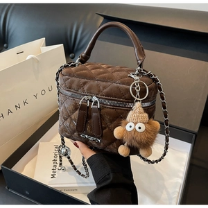 Close-up of brown quilted vanity bag with chain strap and plush monster charm