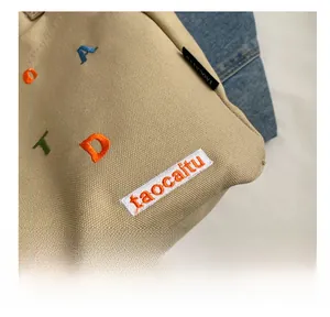Close-up of beige canvas tote bag with colorful letter embroidery and fine texture details