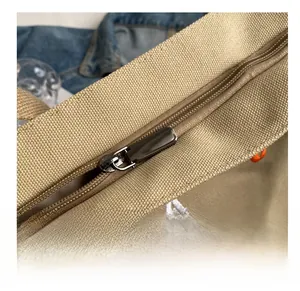 Detail of smooth gunmetal zipper and colorful embroidered letters on khaki canvas tote bag