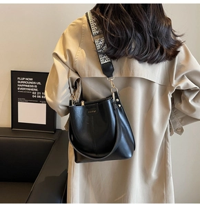 Detail of black leather bucket bag featuring a woven wide strap and golden hardware