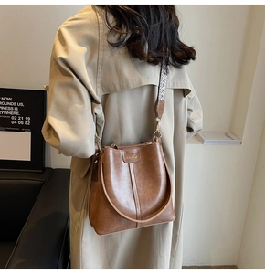 Sac seau rétro marron avec large bandoulière jacquard porté par un mannequin dans une pièce
