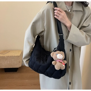 Close-up of black quilted nylon bag featuring a plush teddy bear charm and rhombus pattern
