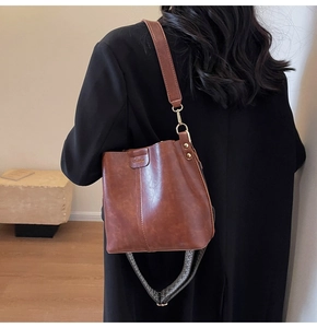 Close-up of caramel brown leather bucket bag with wide fabric strap and gold hardware