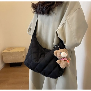 Detail of black quilted nylon tote bag featuring a cute teddy bear charm on shoulder strap