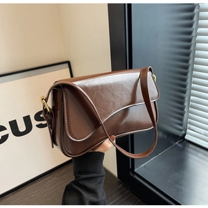Detail of dark brown glossy leather underarm bag with gold buckle and sleek shoulder strap