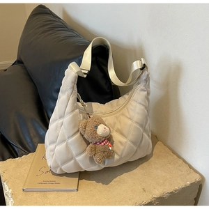 Detail of cream quilted nylon tote bag with a cute teddy bear charm on stone surface