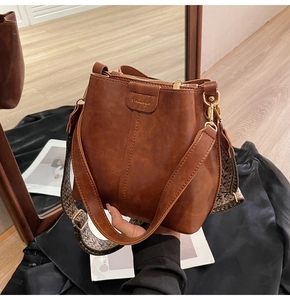 Close-up of brown leather bucket bag featuring a vintage jacquard wide shoulder strap