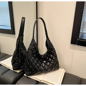 Detail of black quilted puffer tote bag on a book showing glossy nylon texture