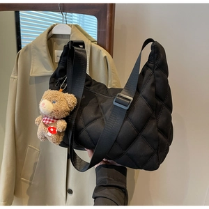 Detail of black quilted nylon tote bag with a cute plush bear charm on a trench coat