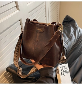 Close-up of brown vintage bucket bag featuring a wide geometric woven shoulder strap