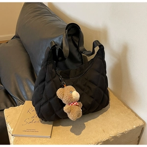 Detailed view of black quilted nylon tote bag with plush bear charm on stone surface