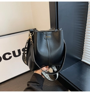 Detail of black leather bucket bag with gold logo and stylish geometric wide strap