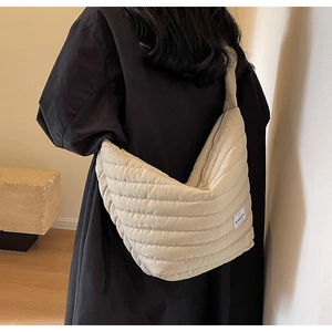 Détail d'un sac demi-lune en nylon matelassé beige porté par un mannequin en vue latérale