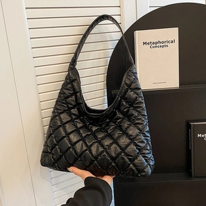 Quilted black tote bag with diamond pattern held against a minimalist background