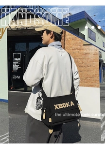 Black canvas messenger bag featuring XBOKA patch and checkered bear charm detail